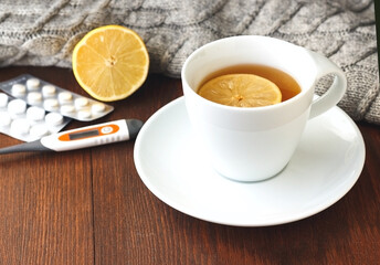 Obraz na płótnie Canvas Pills, thermometer, white cup of hot tea with lemon for colds on wooden background