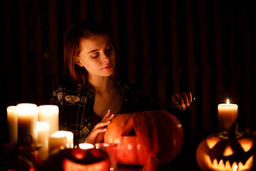 Young woman making Halloween pumpkin Jack-o-lantern with candles in dark. Female hands cutting pumpkins with knife