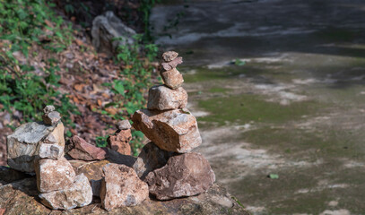 Naklejka premium Balanced stone tower on walkway up the mountain with green plants in the background. No focus, specifically.