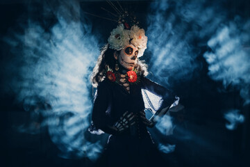 Woman with mexican skull halloween makeup in dark with backlight rays. Day of the dead aka Dia de los Muertos and halloween concept.