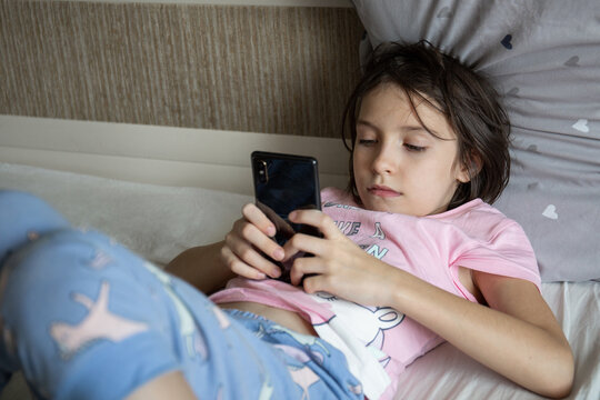 The girl lies in bed in her pajamas and looks at her smartphone. Attachment and addiction to virtual reality.