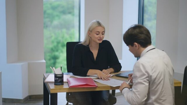 Young smiling woman signing application form with applicant on job interview. Positive Caucasian HR manager talking explaining responsibilities and duties in slow motion