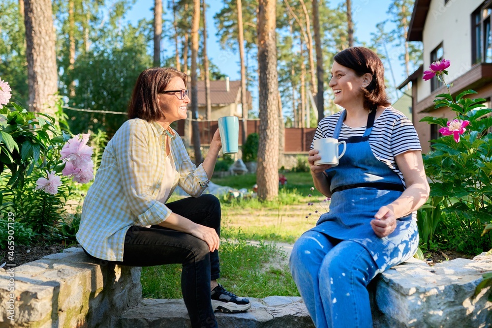 Wall mural Two middle aged women sitting outdoors together in garden, backyard with mugs of tea