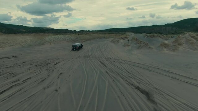 Aerial: 4wd Cars driving on the black sands of Muriwai Beach, Auckland, New Zealand