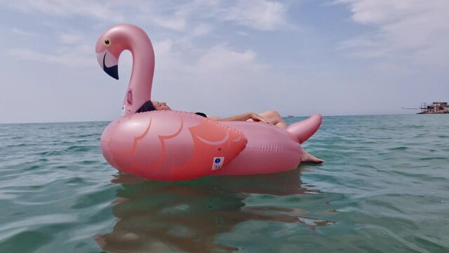 Woman with bikini swimwear relaxing on inflatable pink flamingo floating on sea water surface
