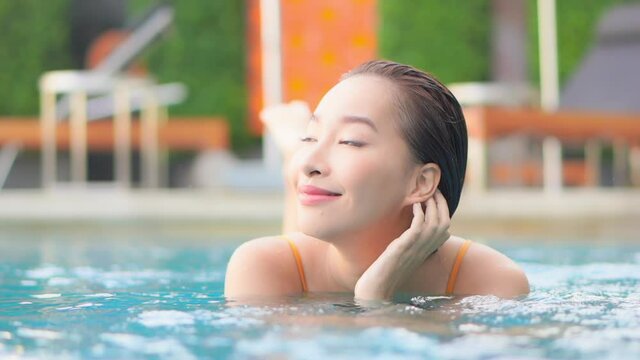 Charming Asian woman relaxing in pool holding face with hand. Slow-motion