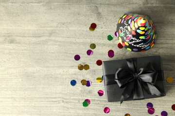 Gift box, party hat and glitter on gray wooden table