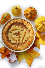 Traditional homemade Apple Pie with fall decoration isolated on white with ornamental pumpkins and fallen leaves