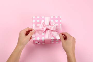 Female hands and gift box with bow on pink background