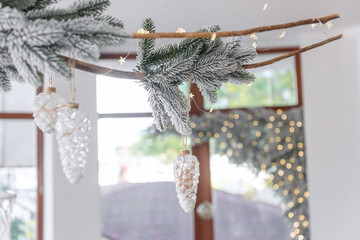 Elegant snow-covered branch of Christmas tree with wooden drift hangs under the white ceiling.