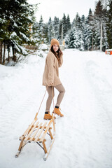 Happy woman with sledge walking among winter forest