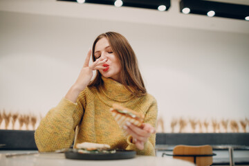 Young european woman lick finger after eating sandwich at indoor cafe. Health and diet.