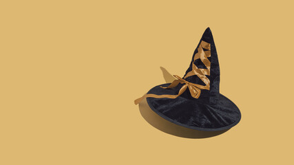 Black color witch’s hat with gold ribbon isolated on golden ocher background. Halloween party...