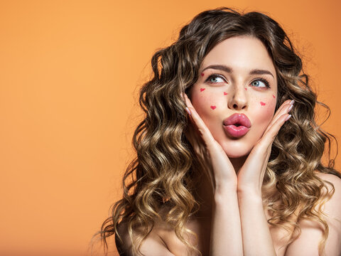 The surprised face of a young girl with bright emotions. Portrait of a beautiful girl with painted red hearts on her face.  An expressive and sensual model with bright makeup poses in the studio.
