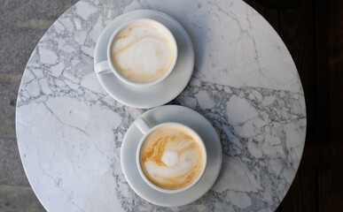 Two cups of cappuccino or latte decorated with foam on marble table background in Coffee shop. Morning coffee for couple in love. Top view. Two white mugs of coffee.