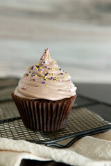 Chocolate muffin with cream and sprinkle on a cooling rack