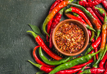 Chili peppers flakes bowl and fresh chili dark background copy space.