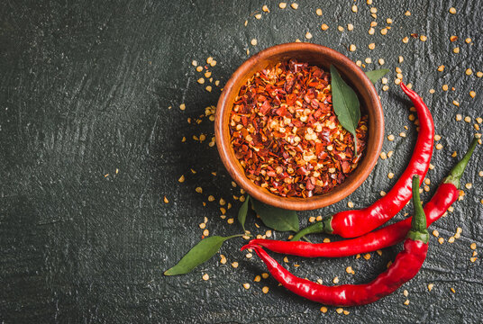 Red chili pepper flakes and fresh chili. Bowl of broken crushed hot red pepper, dried chili flakes top view copy space on dark background.