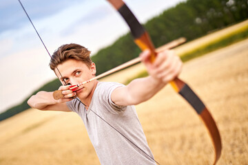 Young male sportsman targeting with traditional bow - Teenager archer practicing archery in nature - Outdoors sports and recreation concept with a millennial boy