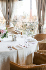 Table setting on the veranda. transparent glasses and white plates on a tablecloth against a background of greenery. Wedding day and holiday atmosphere.