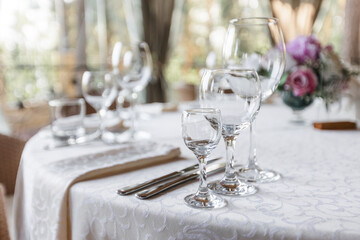 Table setting on the veranda. transparent glasses and white plates on a tablecloth against a background of greenery. Wedding day and holiday atmosphere.