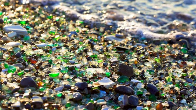 Glass Bay in Vladivostok. Close-up. Multicolored pieces of glass polished by the sea lie on the beach against the backdrop of sea waves. Glass beach.