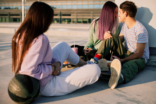 Happy teenage friends are sitting outdoors and hanging after school.