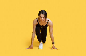 Sprint concept. Young african american female athlete in starting position ready for running, yellow background - obrazy, fototapety, plakaty