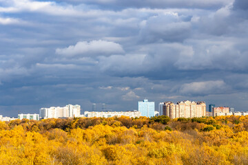 modern urban houses and yellow city park illuminated by sun under dark gray rainy clouds in sky on autumn day before rain