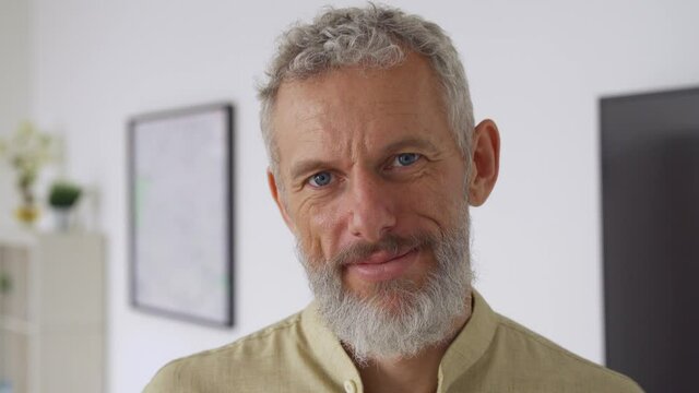 Calm smiling relaxed mature older bearded hipster man looking at camera. Close up portrait of happy handsome confident middle aged 50s male professional, standing at home office posing indoors.