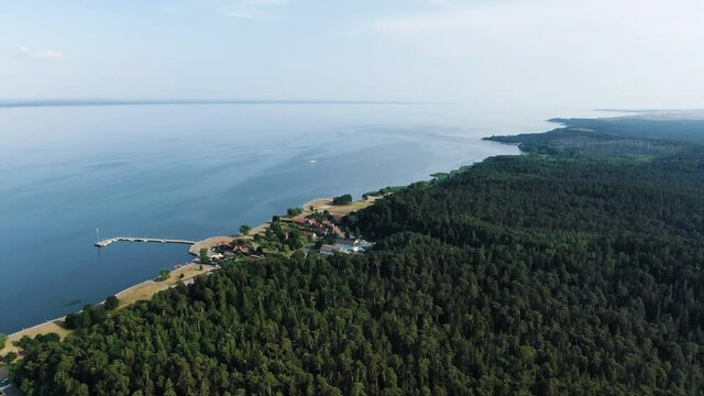 Juodkrante town with small pier surrounded by dense forest and Curonian lagoon, aerial drone view