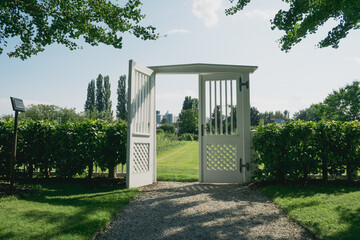 White open gate of a garden with green trees under a clear sky