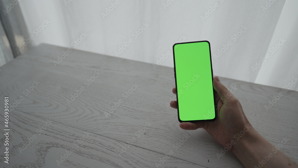 Wall mural man showing and using smarphone with green screen while sitting behind white oak table