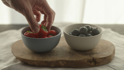 man take fresh strawberries and blueberries in bowls on olive wood board