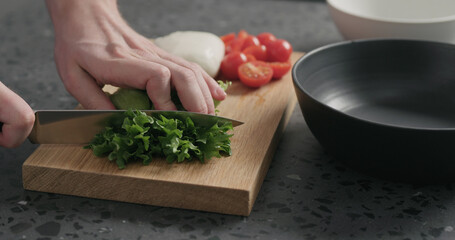 man hands preparing salad with mozzarella, cherry tomatoes and frisee leaves in black bowl on terrazzo surface