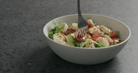 man hand pick salad with mozzarella, cherry tomatoes and frisee leaves in white bowl on terrazzo surface