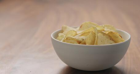 white bowl with black pepper seasoned potato chips on walnut wood table with copy space