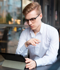 Young handsome blond guy with glasses working or studying in a public place in a cafe