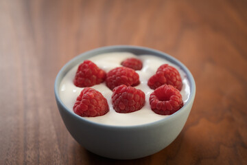 Yogurt with fresh raspberries in blue ceramic bowl on walnut table