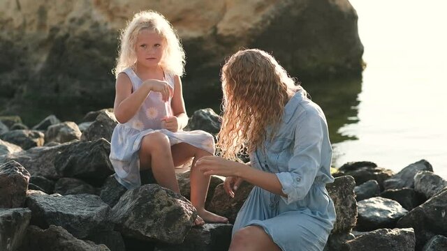 Cute little girl sitting with mommy on the beach and blowing soap bubbles on sunrise