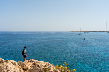 Fototapeta na wymiar Man traveler standing on rock and looking at blue sea. Wanderlust concept.