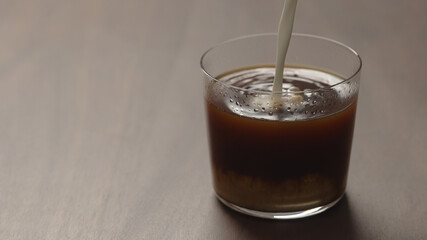 pour cream in coffee in tumbler glass on walnut wood table with copy space