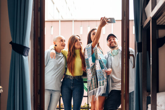 group of young generation z people taking selfies together in balcony outdoor - hostel guests taking pictures with mobile phone