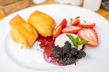 Dessert on a plate with a strudel pie, sweet strawberries and a delicacy of mulberries and whipped cream. Concept of harmful sweet food with excess sugar and calories