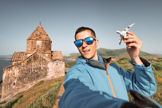 Happy tourist with a toy airplane on the background of a traditional Armenian ancient church and Sevan lake. Concept of air flight transportation