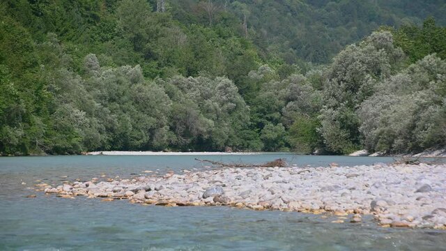 Beautiful and colorful Soča river flowing in pristine alpine valley, Slovenia. Majestic mountains in the distance. Summer day. Curvy clean river in wilderness. Static shot, real time
