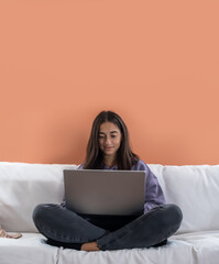 Vertical young teenager girl using laptop studying at home, checking email news online sitting on sofa, searching for friends in internet social networks