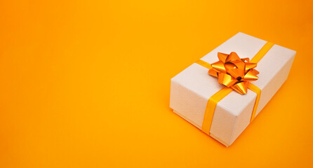    White gift textured box with golden bow on yellow background. Christmas, New Year, Birthday, shopping sales concept.