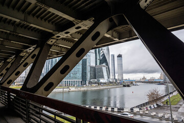 view of modern buildings made of glass and concrete through the spans of an old iron bridge with forged details 