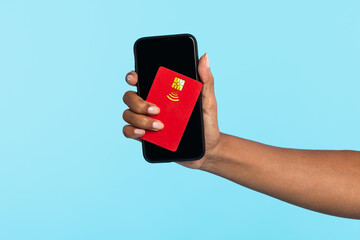 Unrecognizable millennial black woman holding credit card and cellphone on blue background, mockup for design